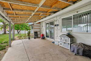Concrete patio with an exposed wood ceiling structure, sliding glass door access, and a large window with vertical blinds