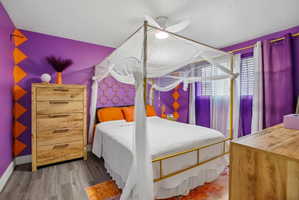 Bedroom featuring wood-finish flooring, a ceiling fan, and two windows with blinds and curtains