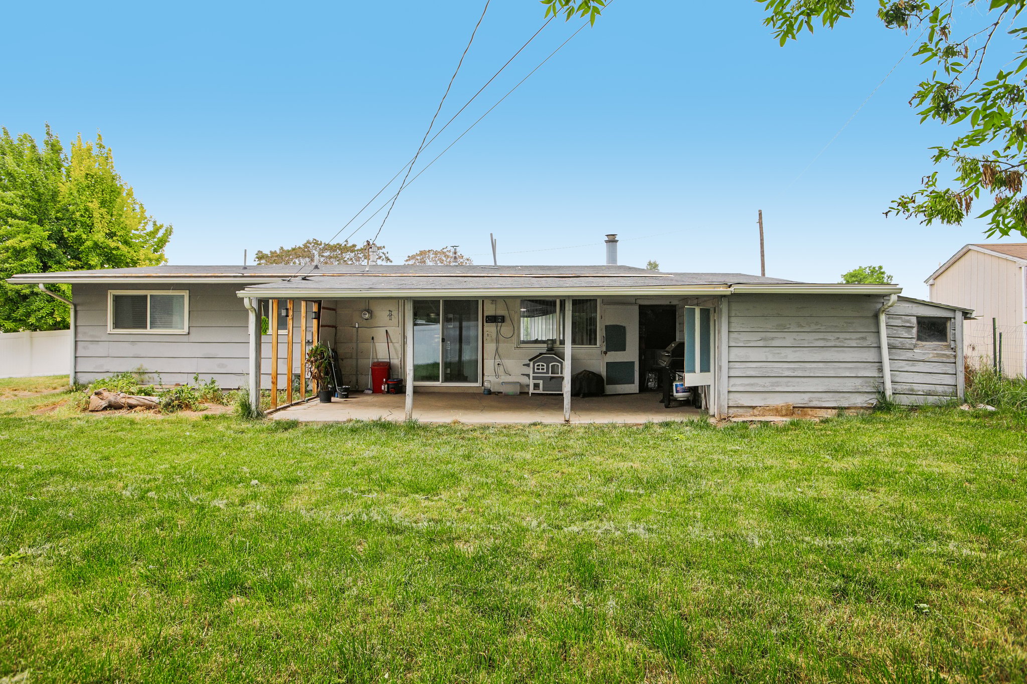 Expansive rear lawn featuring a covered concrete patio, sliding glass door access, and an attached storage shed