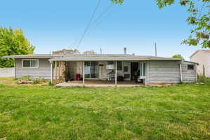 Expansive rear lawn featuring a covered concrete patio, sliding glass door access, and an attached storage shed
