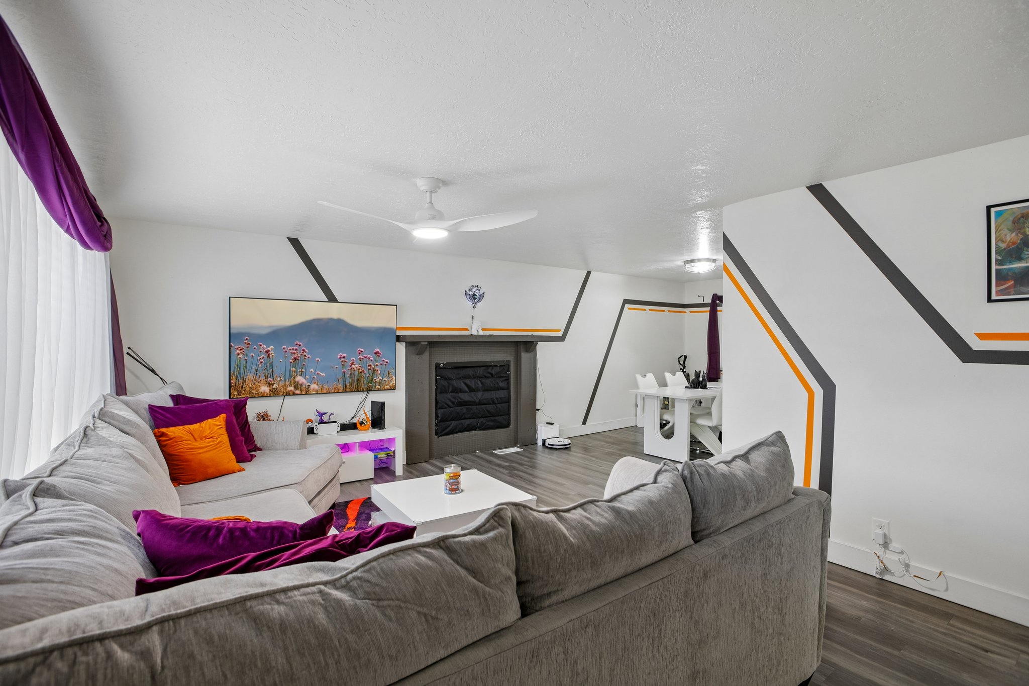 Living room featuring wood-finish flooring, a ceiling fan with integrated lighting, a fireplace with a dark mantel, and white walls with decorative accents