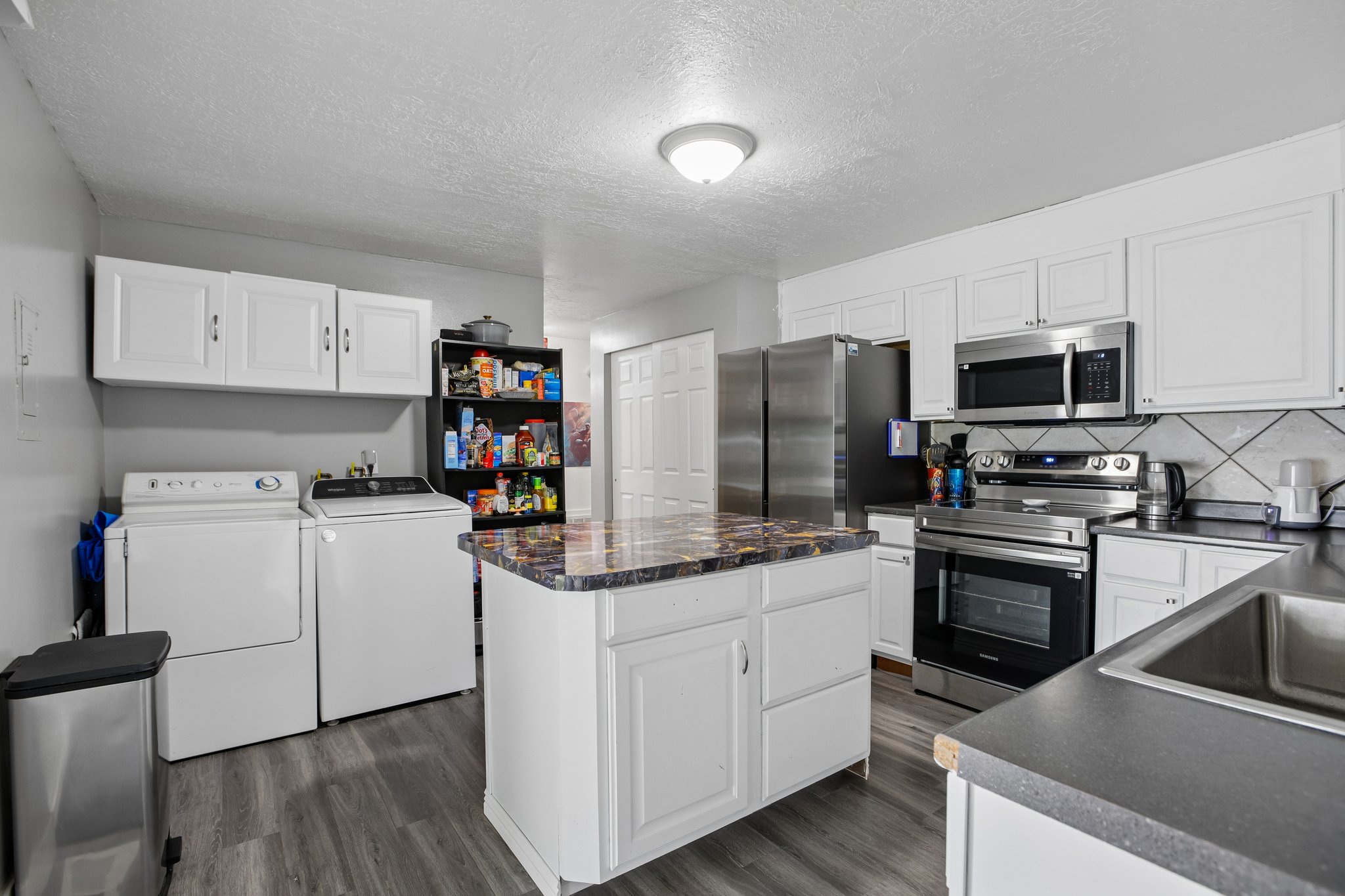 Kitchen featuring white cabinetry, gray wood-finish flooring, a central island with a multi-toned countertop, stainless steel appliances, and a tile backsplash