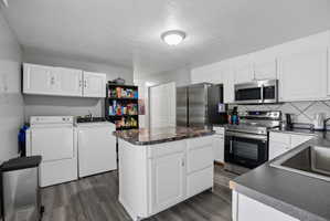 Kitchen featuring white cabinetry, gray wood-finish flooring, a central island with a multi-toned countertop, stainless steel appliances, and a tile backsplash