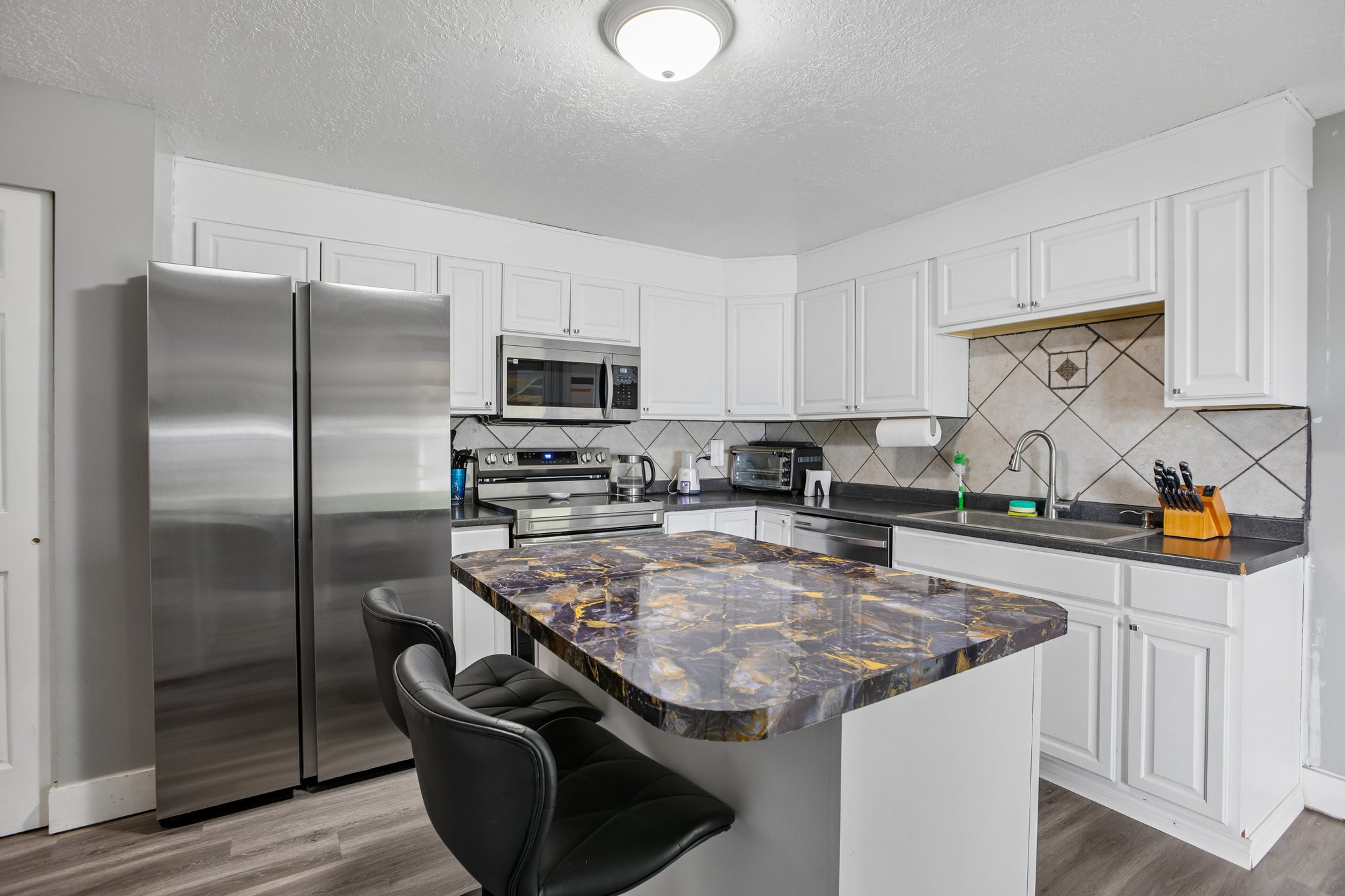 Kitchen featuring a central island with a multi-toned countertop, white cabinetry, stainless steel appliances, a tiled backsplash, and wood-finish flooring