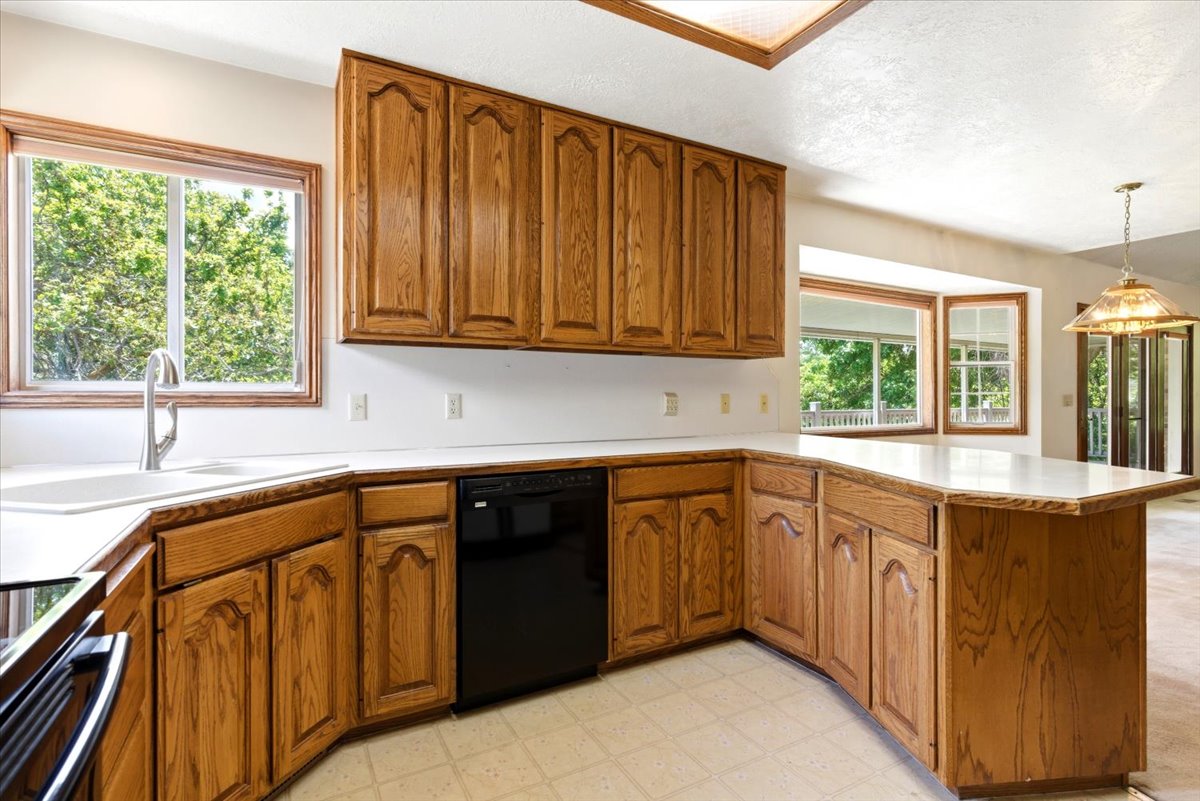 Kitchen featuring wood cabinetry, white countertops, a black dishwasher, and a stainless steel sink with a gooseneck faucet
