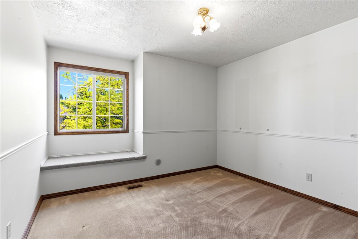 Room featuring a large window with wood-finish trim, a window seat with a textured surface, and a three-light ceiling fixture
