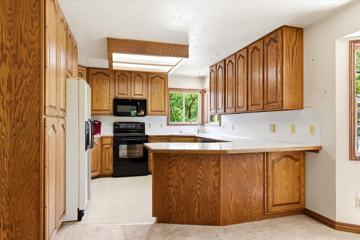 Expansive kitchen featuring abundant wood cabinetry, white countertops, black appliances, and a built-in breakfast bar