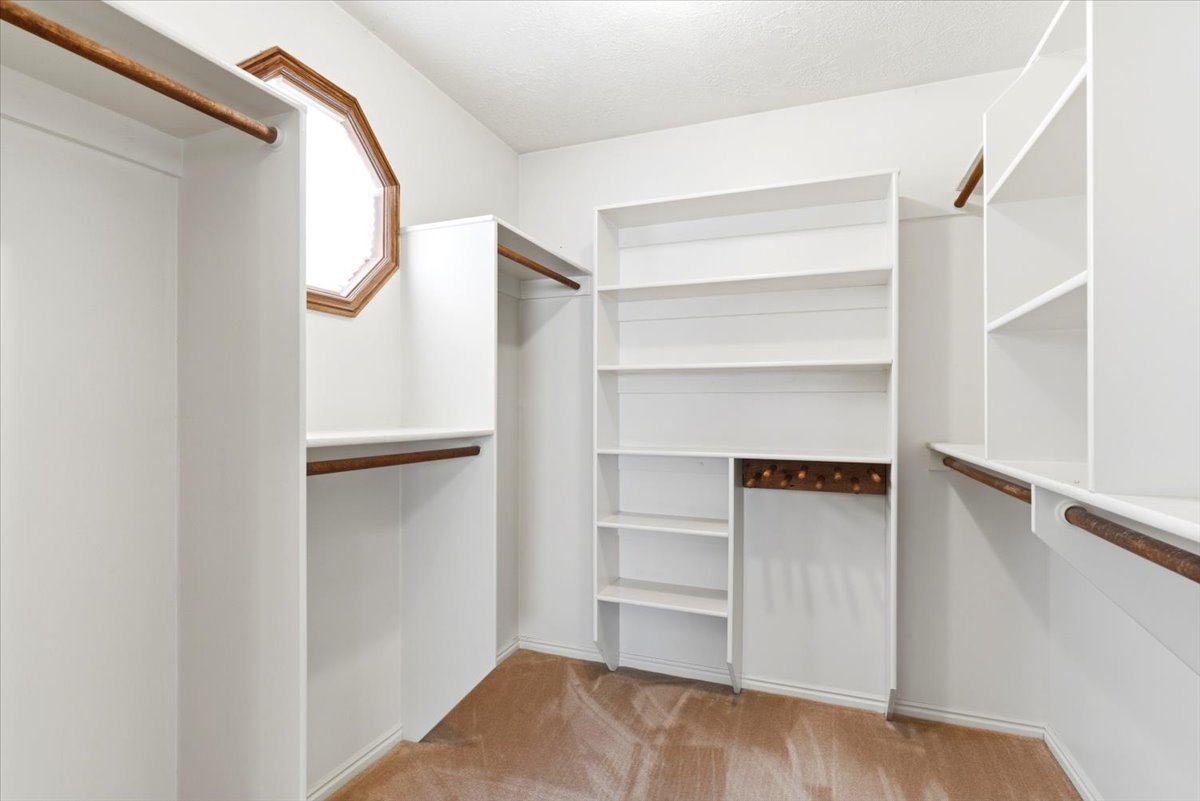 Walk-in closet featuring built-in shelving, hanging rods, and an octagonal window with wood trim