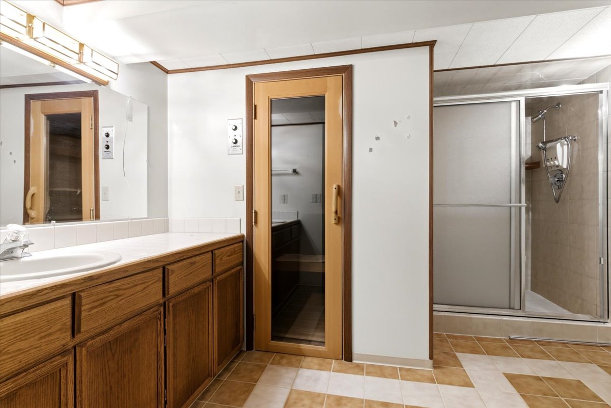 Bathroom featuring a wood-finish vanity with an integrated sink and white countertop, a mirrored wall, a glass-enclosed shower, and a built-in sauna with a glass door
