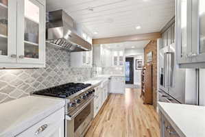 Modern kitchen featuring stainless steel appliances, white cabinetry, a patterned backsplash, light-toned wood-finish flooring, and white countertops