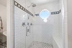 Tiled shower enclosure featuring a frameless glass door, octagonal window, built-in bench, showerhead, and body sprayers