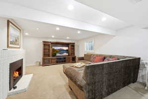 Living area featuring a white brick fireplace with a tile hearth, recessed lighting, and neutral carpeting
