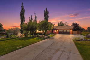 Brick exterior home featuring a concrete driveway, attached garage with panel doors, shingled roof, and mature landscaping with large rocks