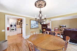 Open-concept dining area featuring a decorative chandelier with an ornate ceiling medallion, wood-finish flooring, and a cased opening revealing a kitchen with stainless steel appliances
