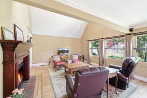 Living area featuring vaulted ceilings, wood-finish flooring, a prominent fireplace with a substantial wood mantel, and multiple windows
