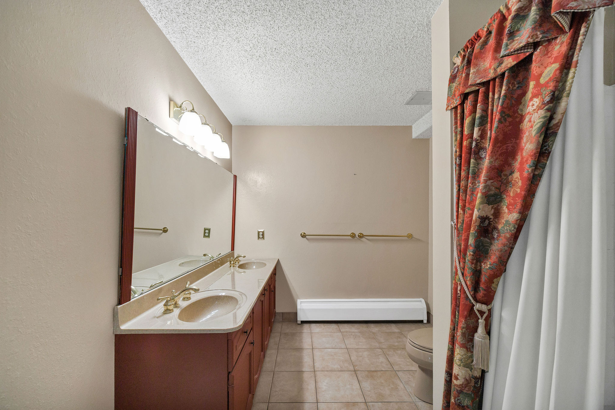 Bathroom featuring a double vanity with integrated sinks, a lengthy mirror, overhead light fixture, and tile flooring