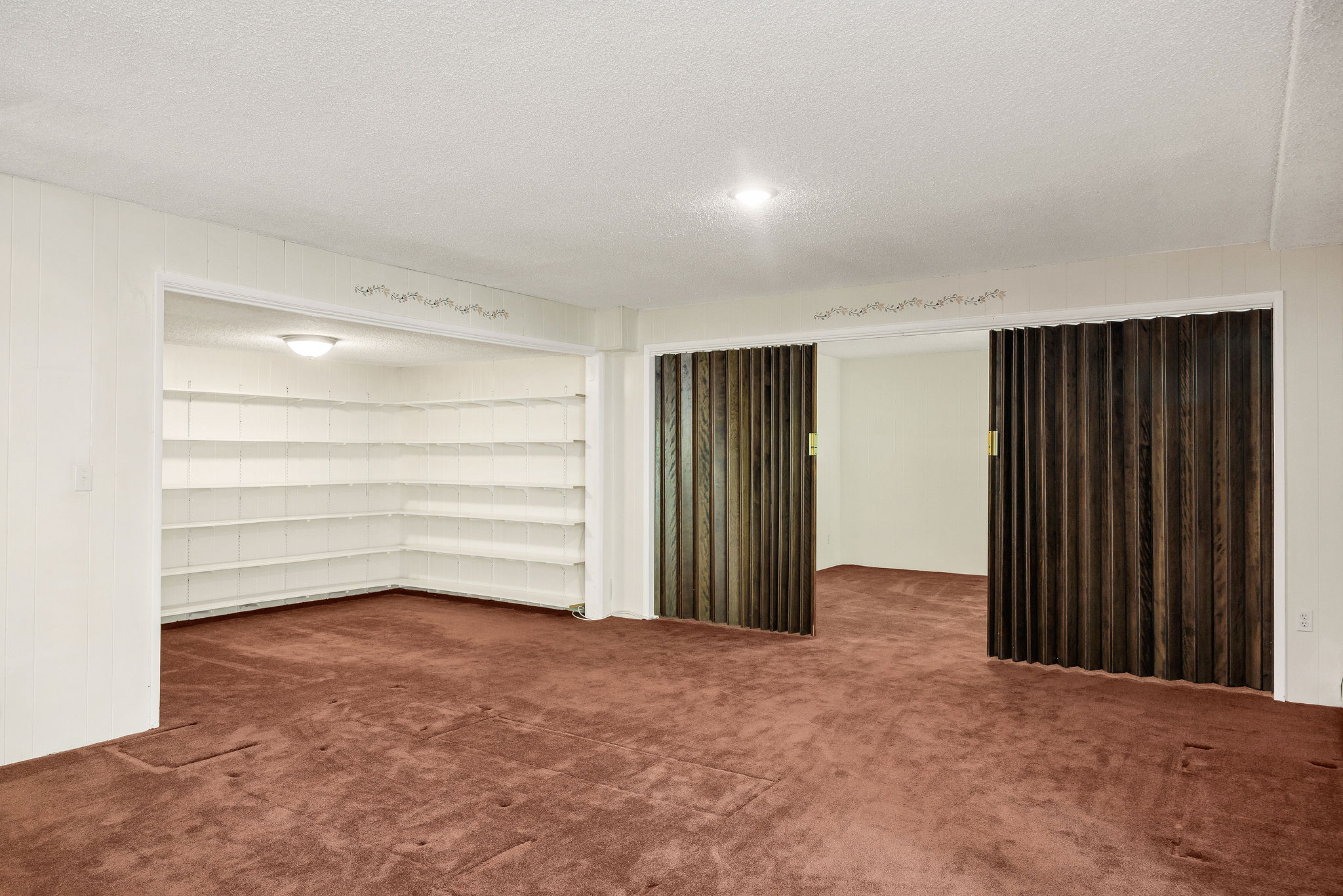 Spacious room with plush carpeting, featuring built-in shelving, a recessed ceiling light, and bi-fold wood-finish doors
