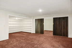 Spacious room with plush carpeting, featuring built-in shelving, a recessed ceiling light, and bi-fold wood-finish doors