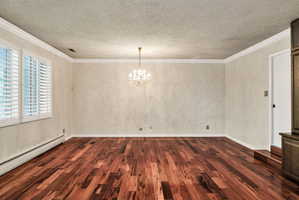 Hardwood flooring throughout featuring white plantation shutters, a crystal chandelier, crown molding, and textured wall coverings