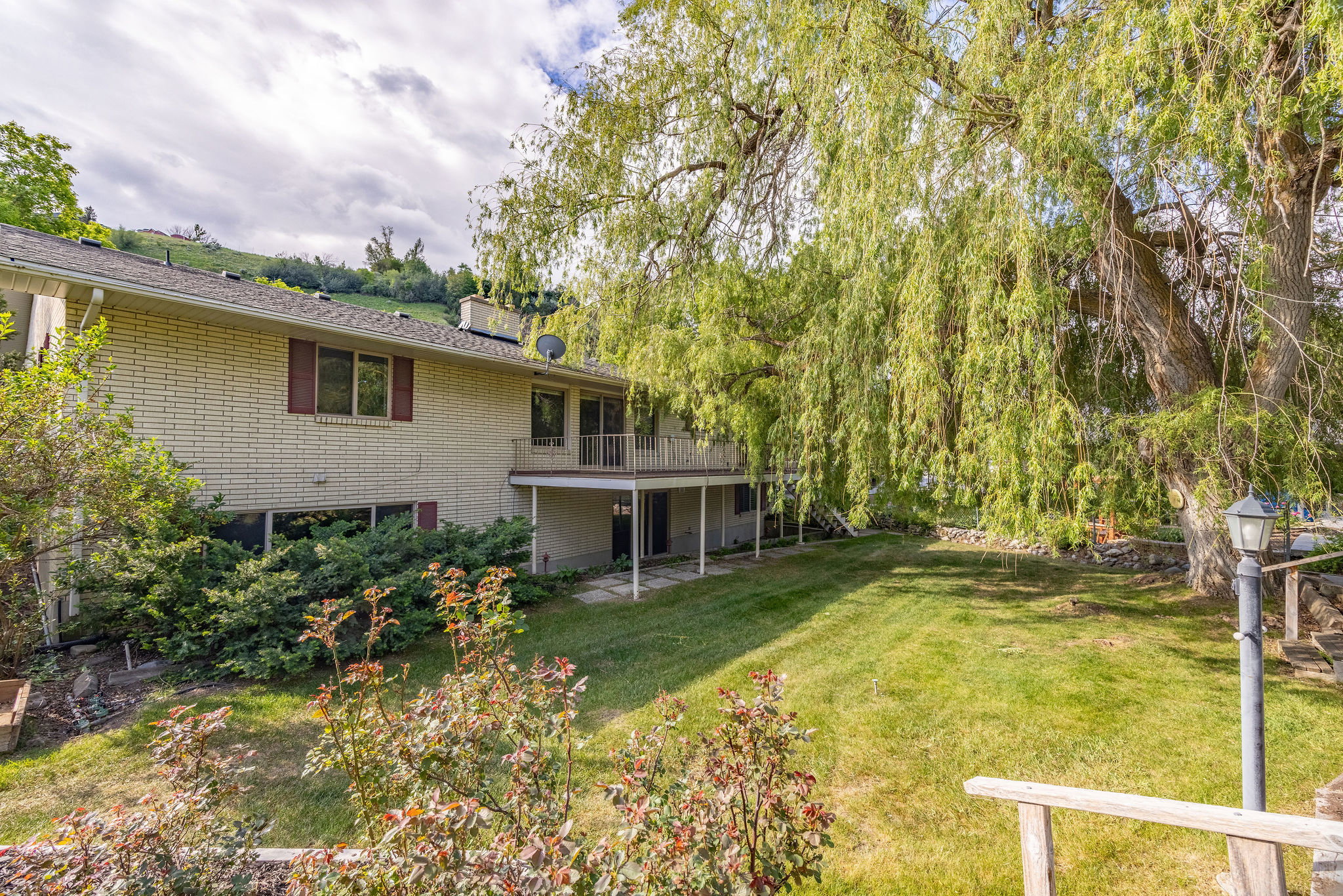 Rear exterior featuring a brick facade, upper-level balcony, and lower-level patio with stone pavers