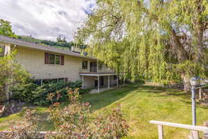 Rear exterior featuring a brick facade, upper-level balcony, and lower-level patio with stone pavers