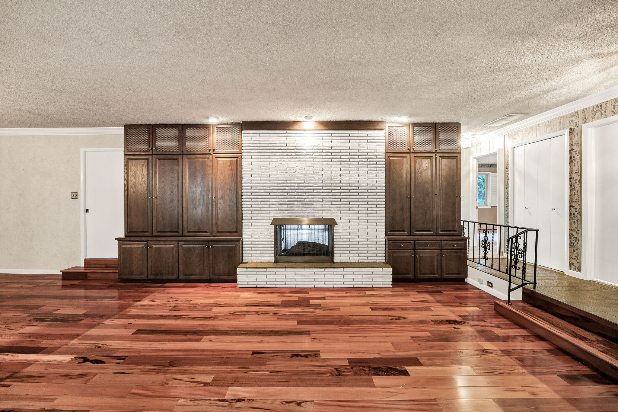 Spacious room featuring wood-finish flooring and a central fireplace with a white brick surround and hearth