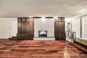 Spacious room featuring wood-finish flooring and a central fireplace with a white brick surround and hearth