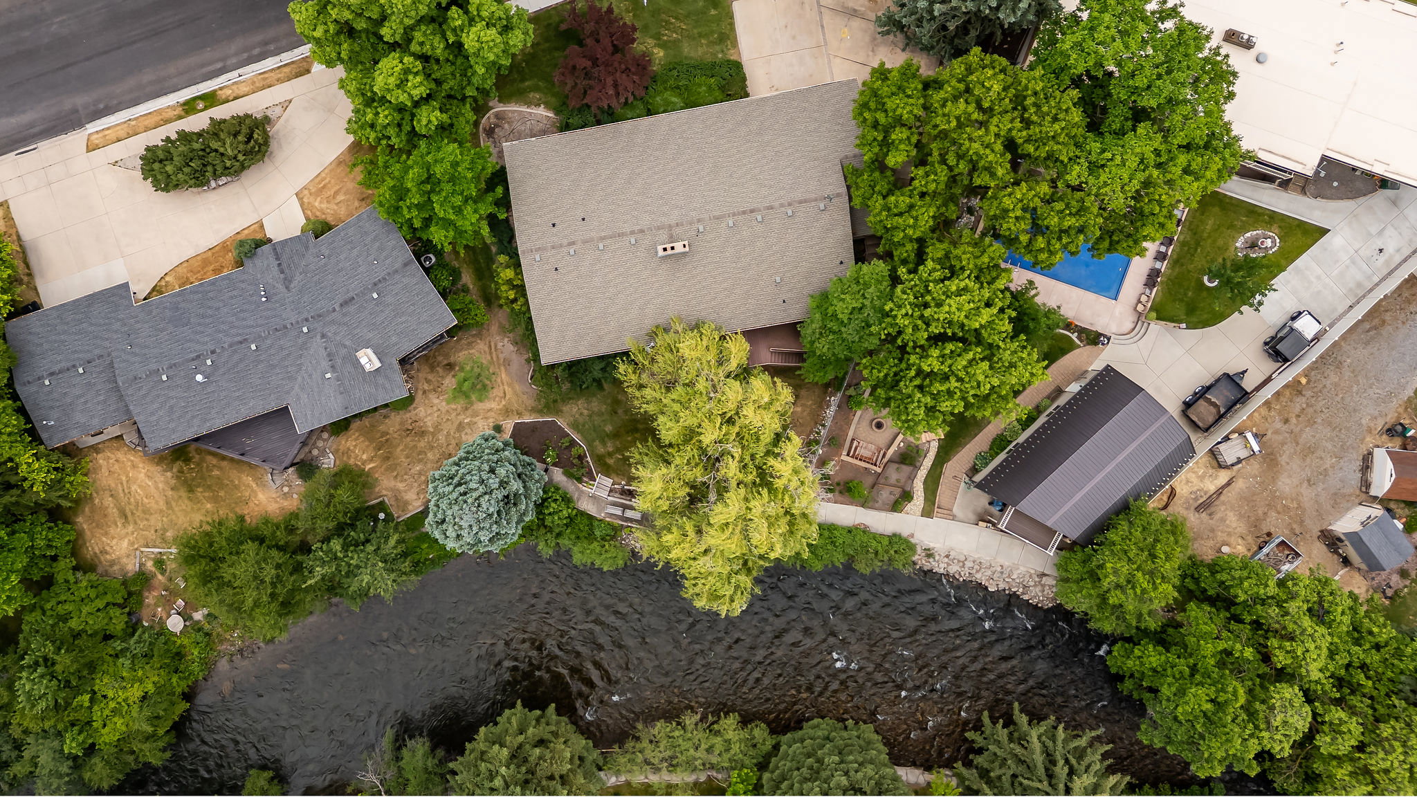 Riverside property featuring a main residence with a gabled roof, an auxiliary structure with a dark metal roof, a pool, and mature trees
