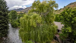 Riverside property with mature trees, a multi-level deck, and a pitched roof, set against a mountainous backdrop