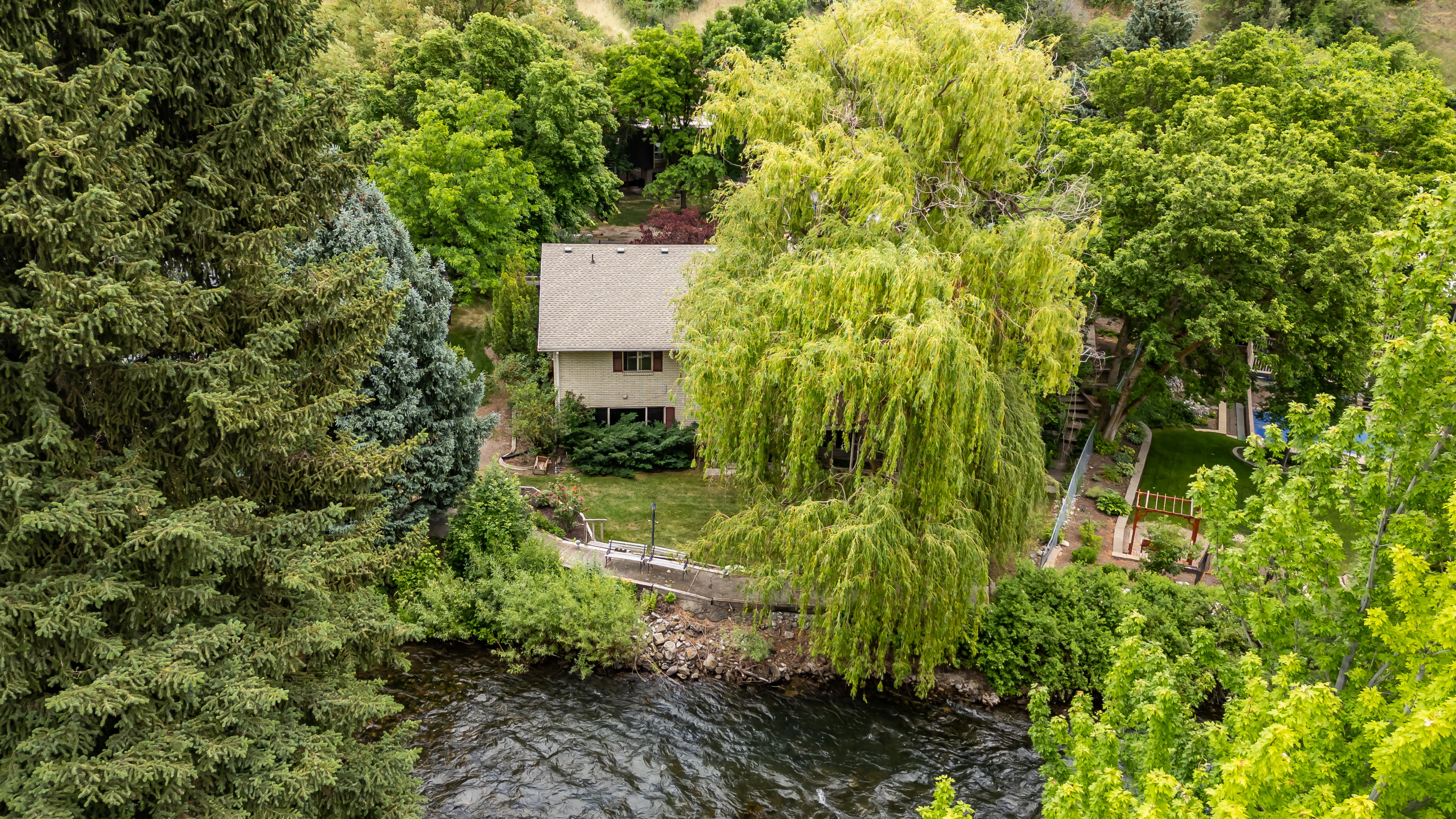 Two-story residence with a light-toned exterior and a gabled roof, nestled among abundant mature trees