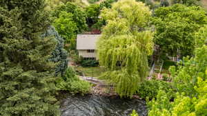 Two-story residence with a light-toned exterior and a gabled roof, nestled among abundant mature trees