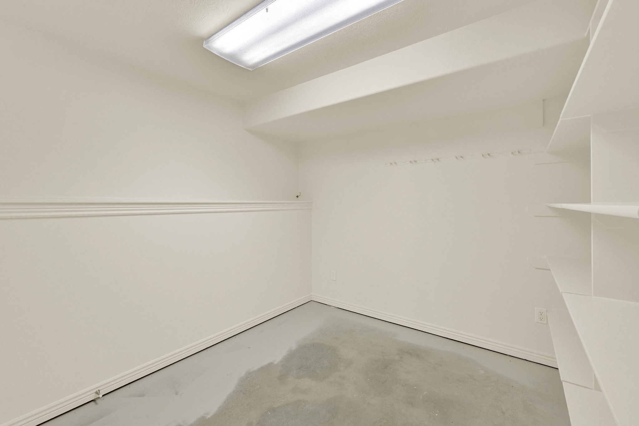 Utility room featuring built-in shelving, wall-mounted hooks, baseboard trim, and overhead fluorescent lighting