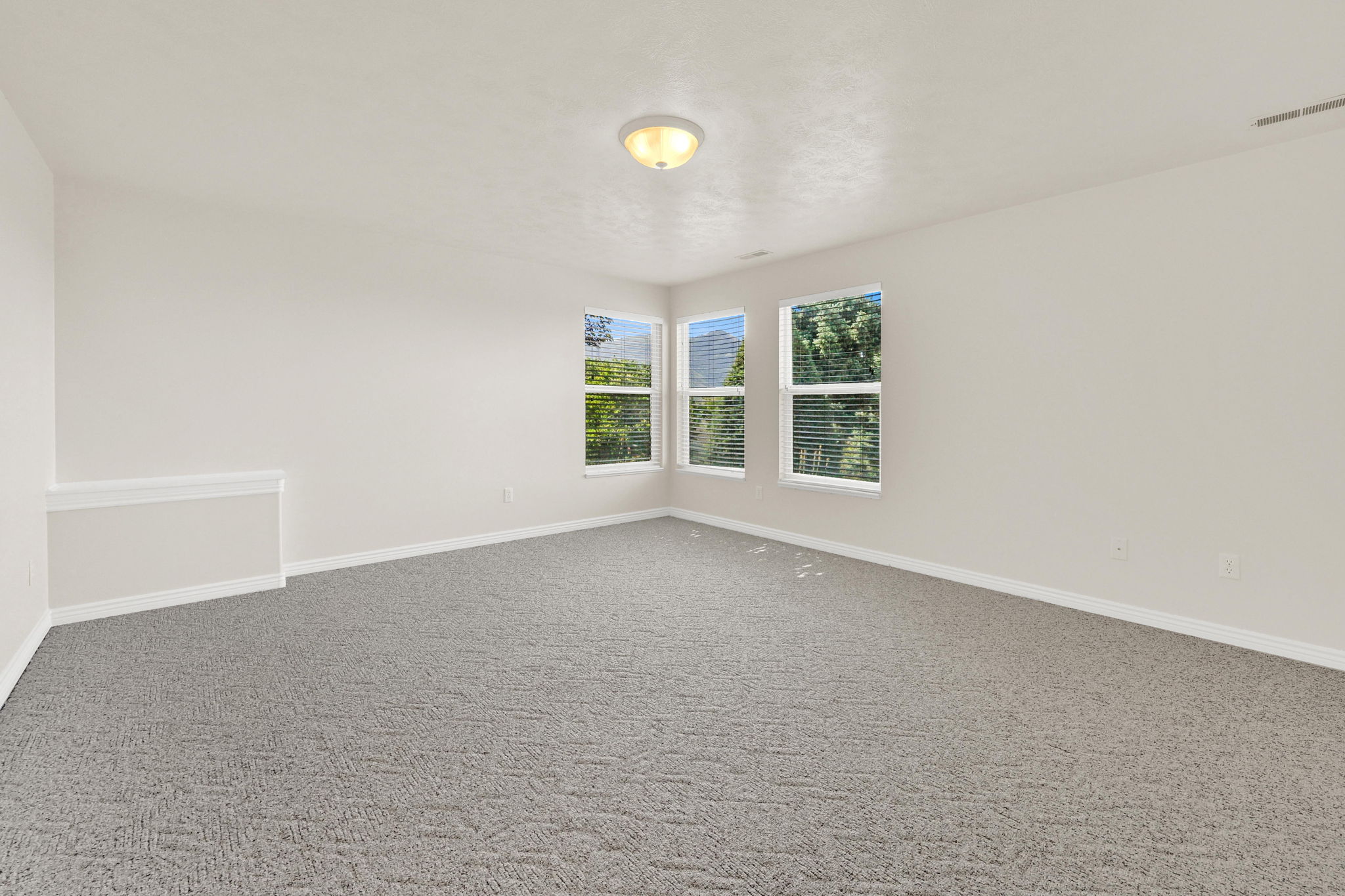 Spacious interior featuring three windows, neutral wall tones, and gray patterned carpeting