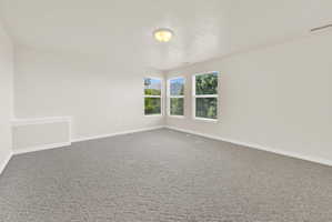 Spacious interior featuring three windows, neutral wall tones, and gray patterned carpeting