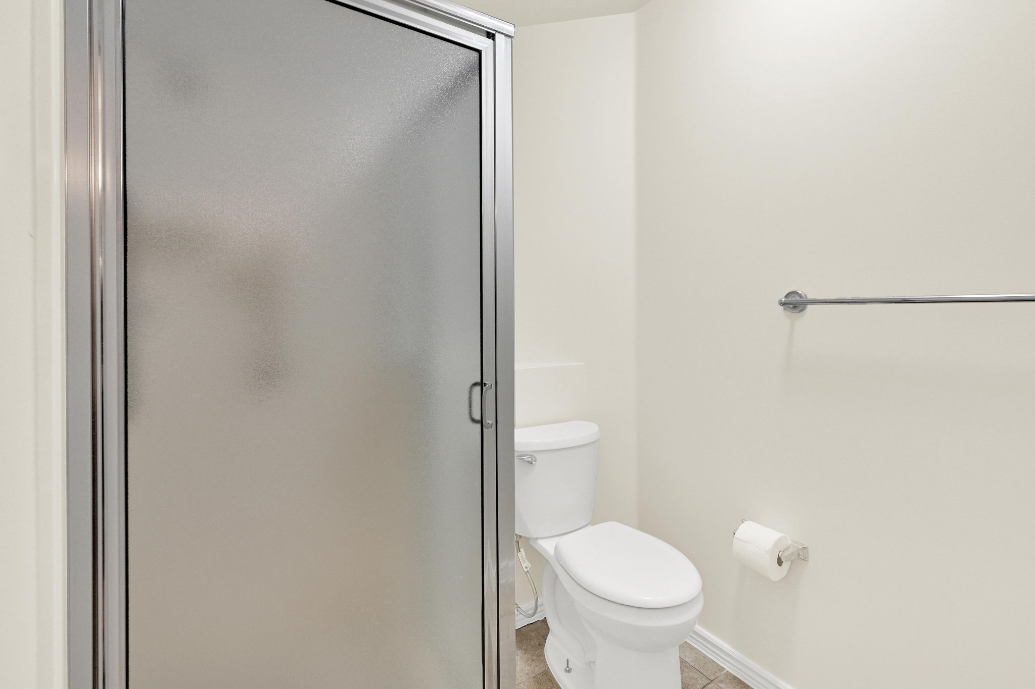 Frosted glass shower enclosure with chrome framing, white toilet, and tile flooring