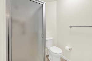 Frosted glass shower enclosure with chrome framing, white toilet, and tile flooring