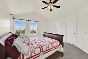 Vaulted ceiling room featuring a decorative ceiling fan with integrated lighting, two windows with white plantation shutters, and light-colored carpeting