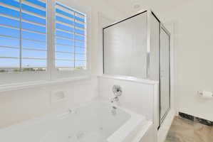 White jetted soaking tub with chrome fixtures, plantation shutters, and an enclosed standing shower with frosted glass panels