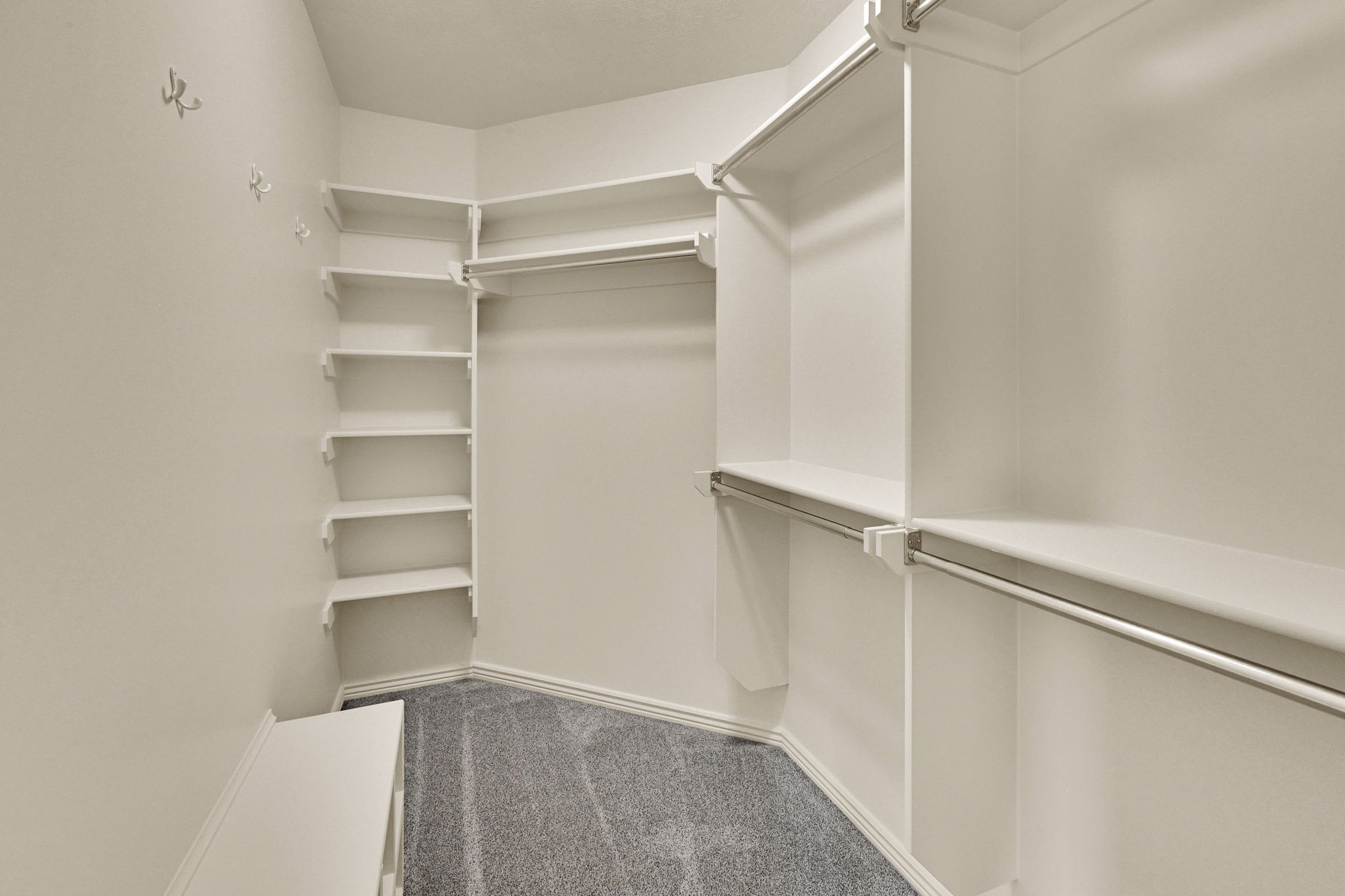 Walk-in closet featuring built-in shelving, multiple hanging rods, and grey carpeting