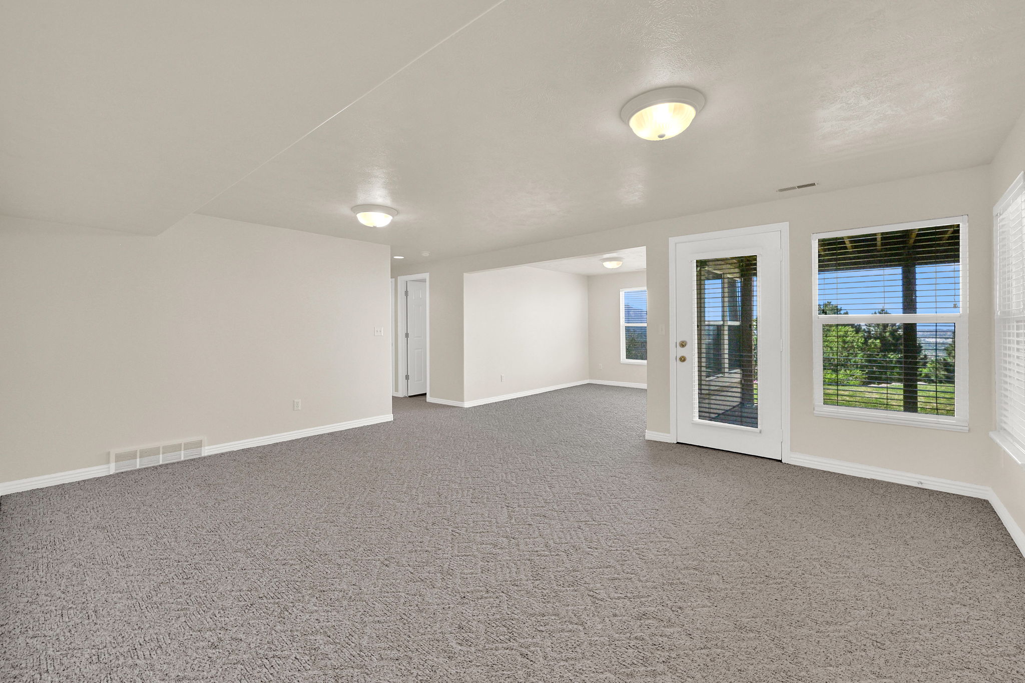 Spacious room with grey patterned carpeting, light neutral wall paint, and white trim