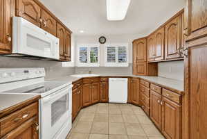 U-shaped kitchen featuring wood cabinetry, white appliances, and tiled flooring