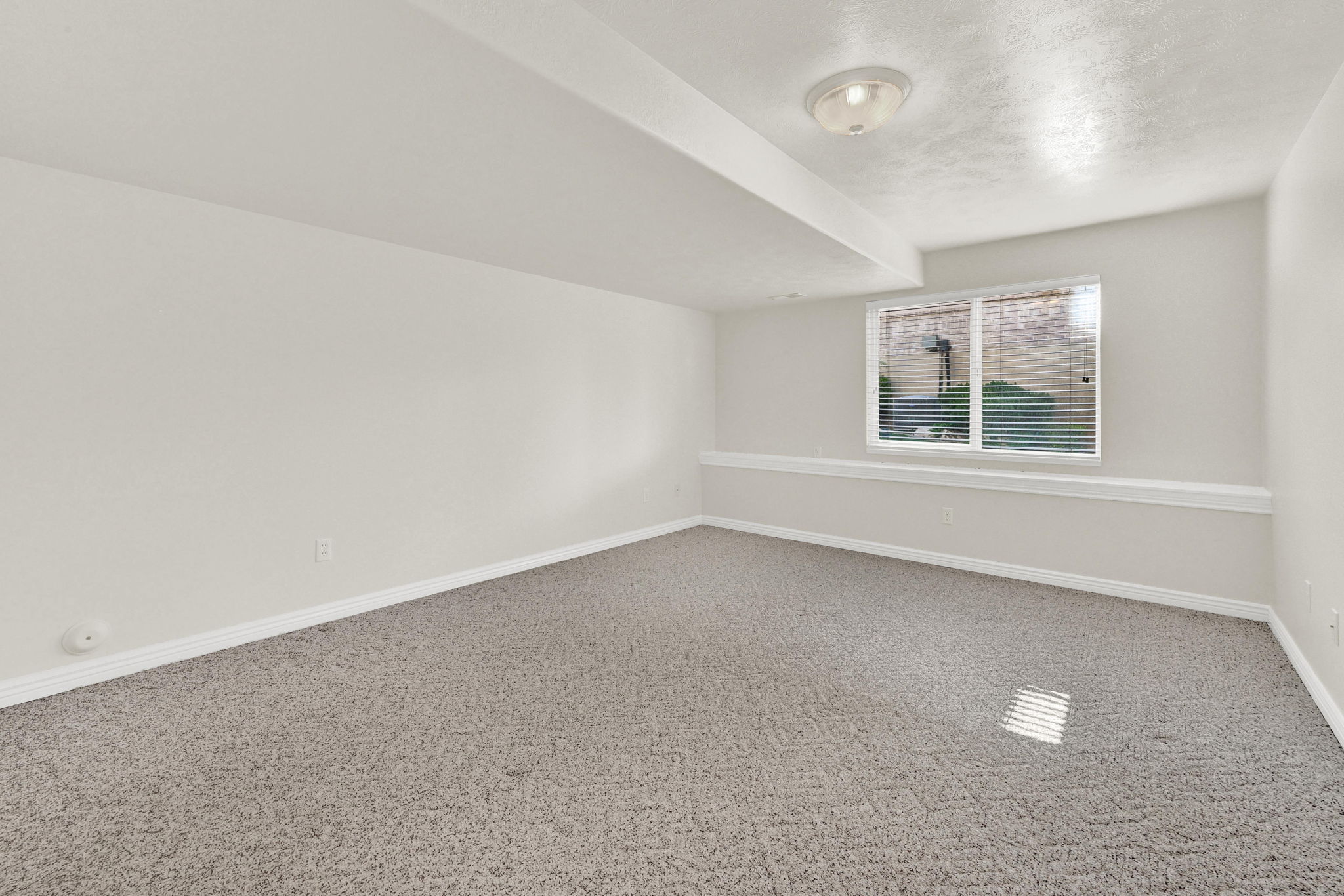 Carpeted interior space featuring neutral wall tones, a recessed window with horizontal blinds, overhead flush mount lighting, and a partial decorative chair rail