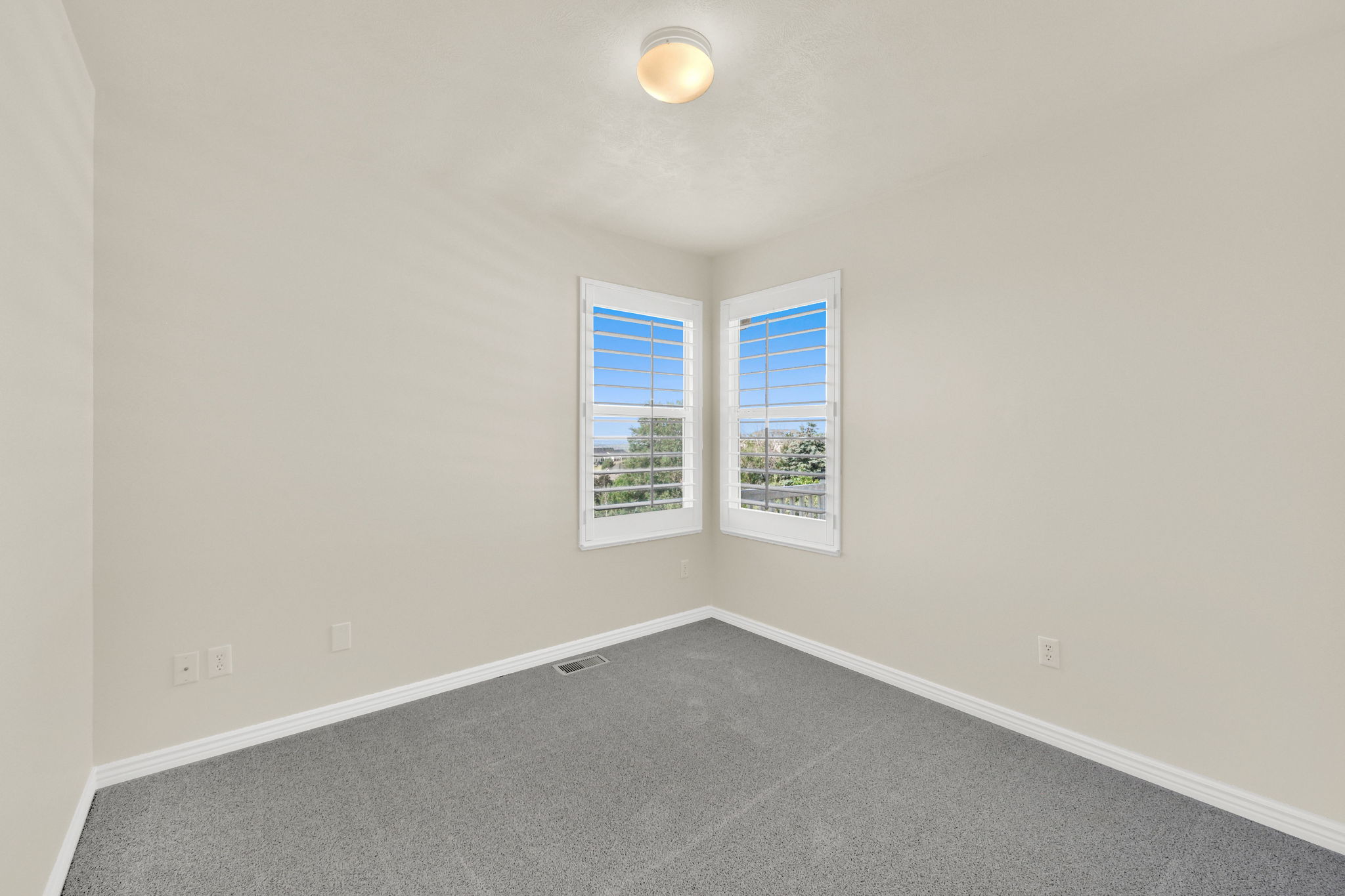 Corner windows with plantation shutters, light-toned walls, and grey carpeting