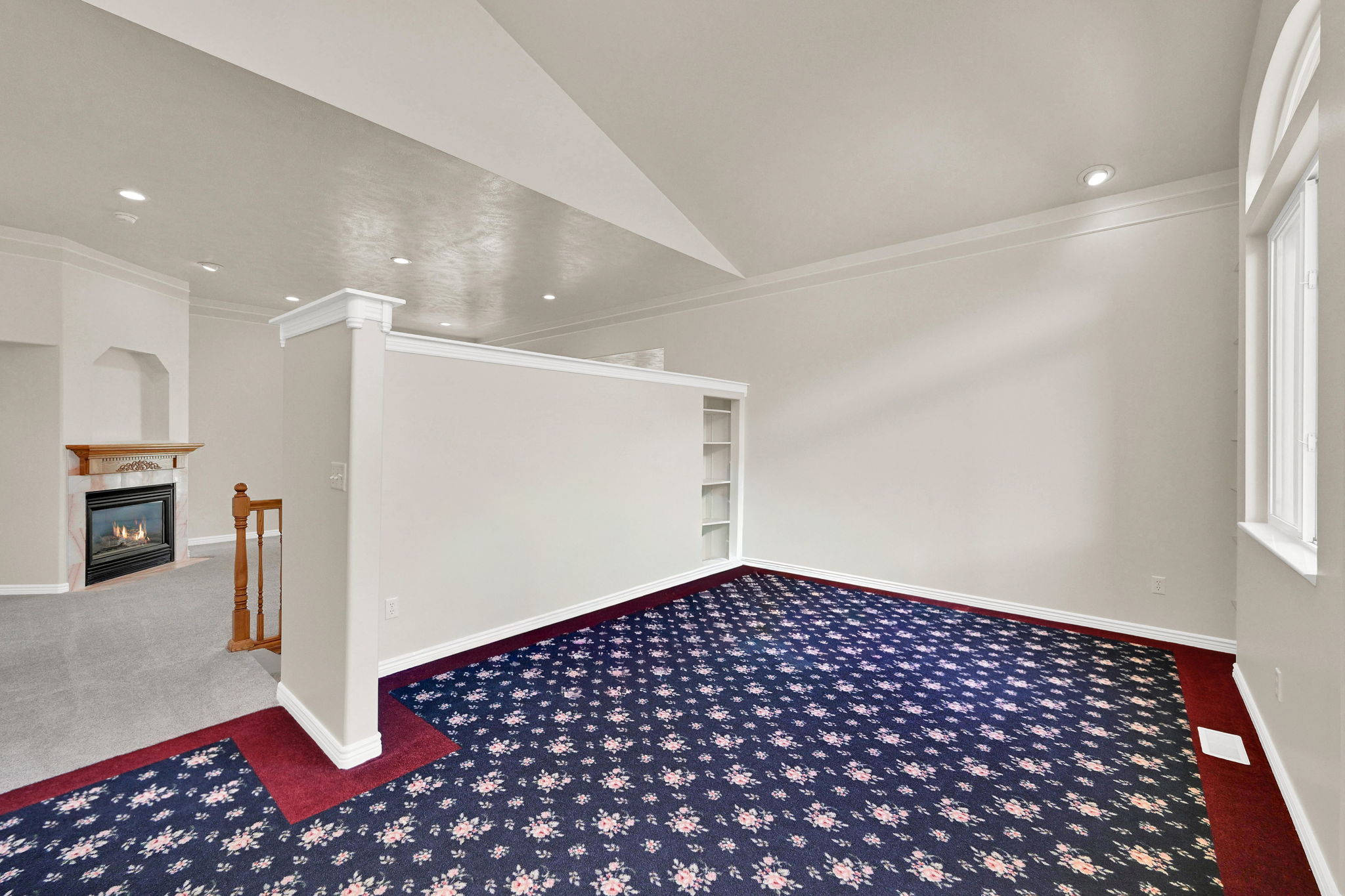 Spacious room with patterned carpeting, white walls, and a built-in bookshelf