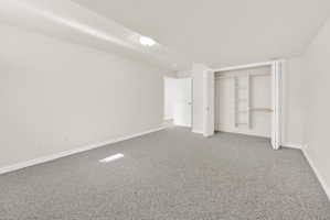 Spacious room featuring light gray carpeting, white walls, white baseboards, and a built-in closet with shelving and hanging rods