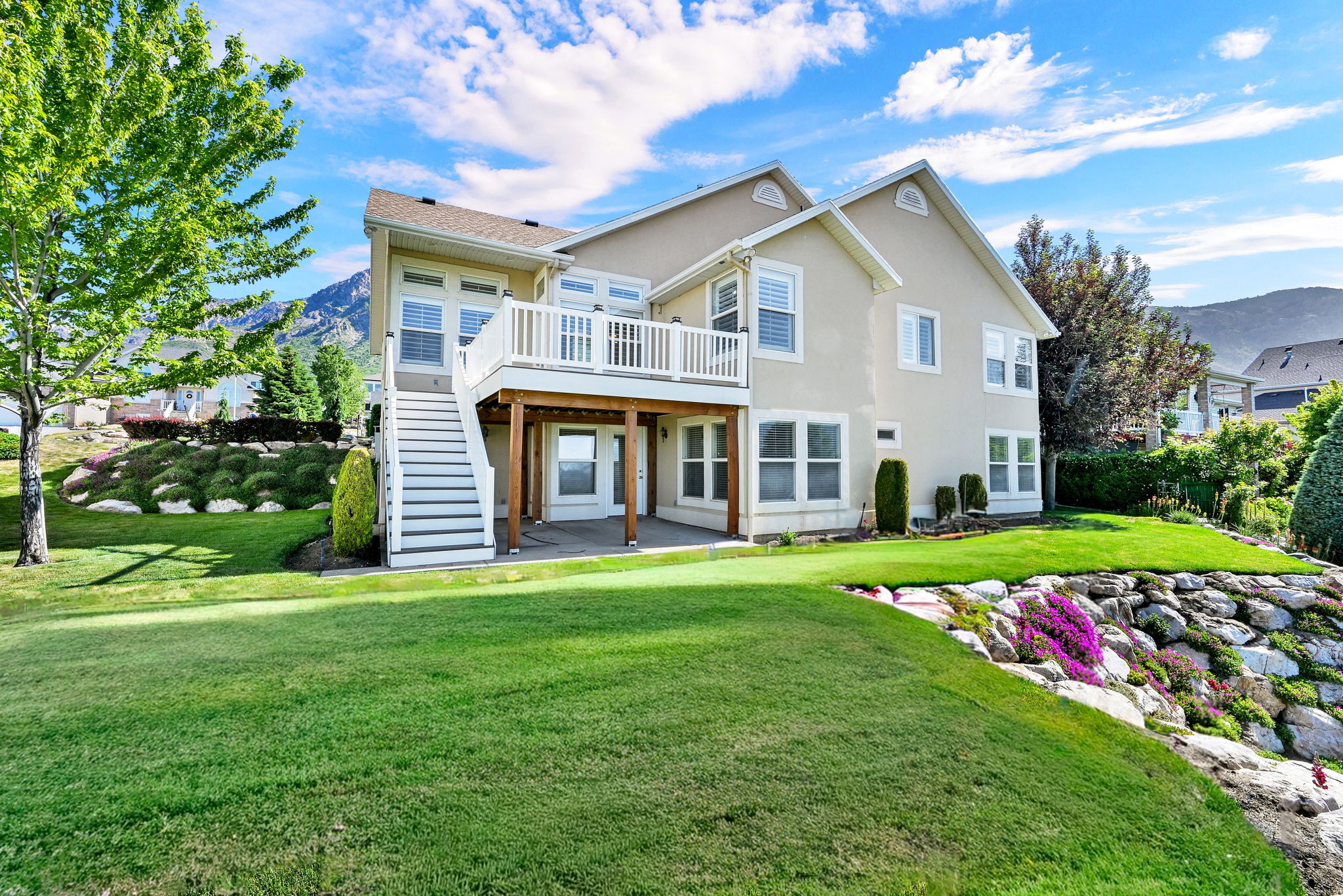 Rear exterior featuring a two-story stucco facade, second-story balcony with white railing, covered patio, and a staircase descending to the lawn