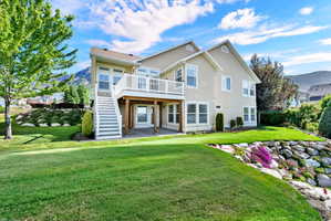 Rear exterior featuring a two-story stucco facade, second-story balcony with white railing, covered patio, and a staircase descending to the lawn