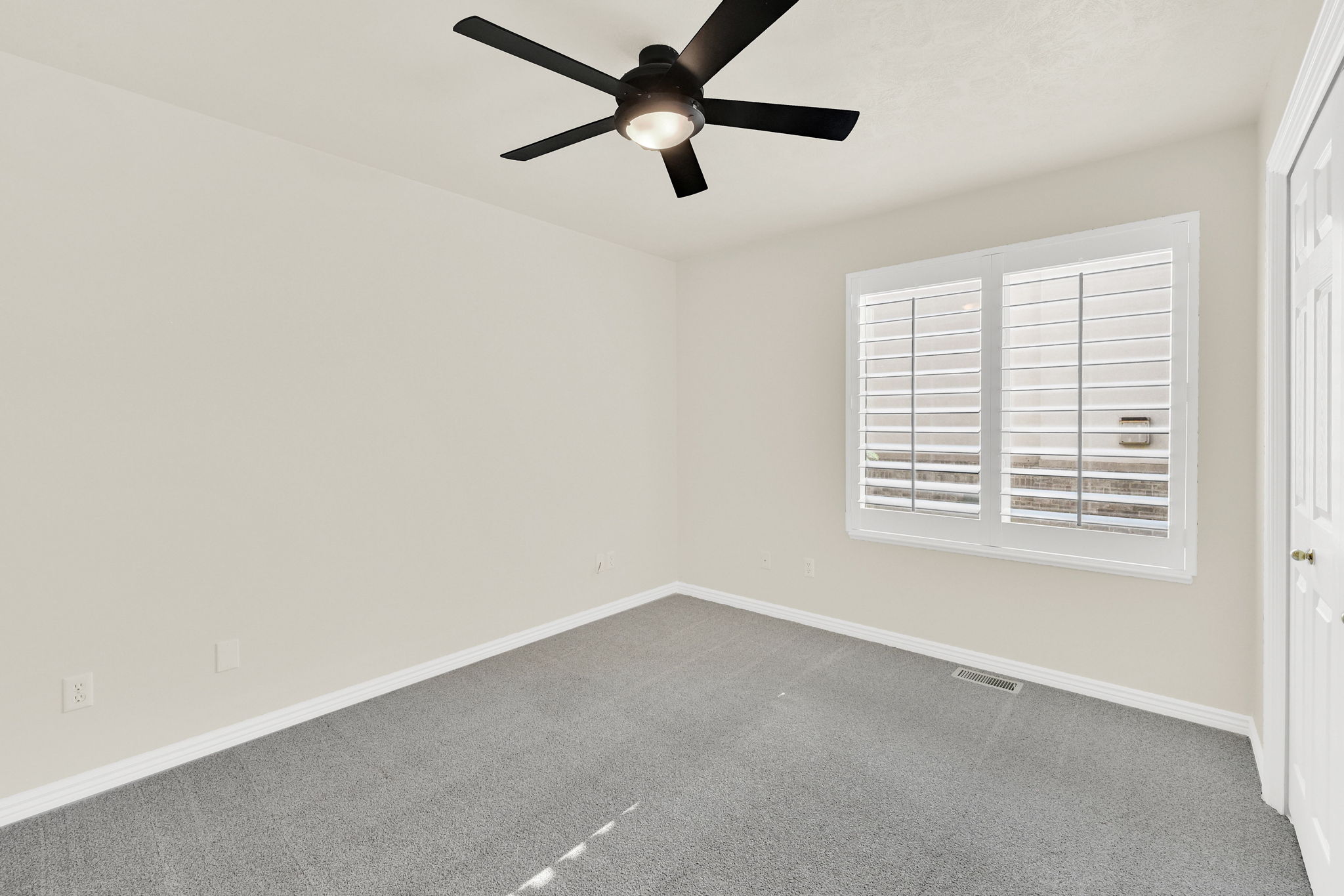 Light-filled room featuring a ceiling fan with light fixture, neutral carpeting, and a window with plantation shutters