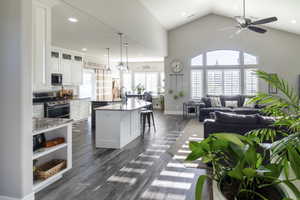 Open-concept living space featuring vaulted ceilings, wood-finish flooring, and white plantation shutters