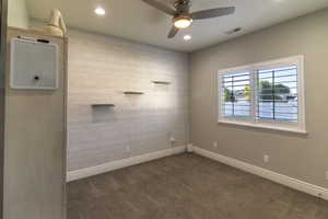 Carpeted room featuring a shiplap accent wall with integrated shelving, a ceiling fan with light fixture, recessed lighting, and a window with plantation shutters
